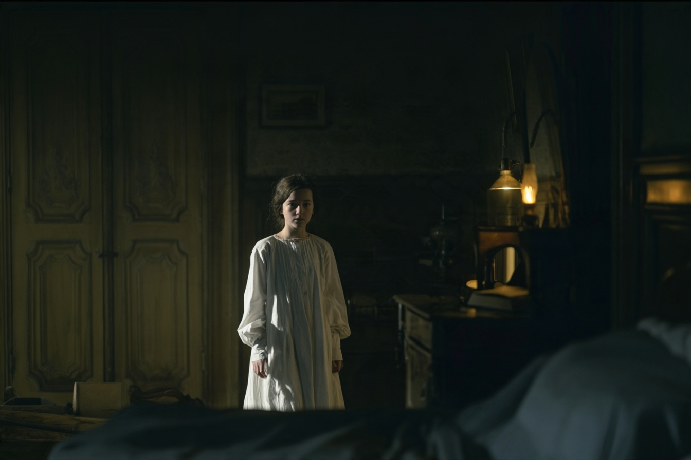 A girl in a white nightgown in a candlelit bedroom